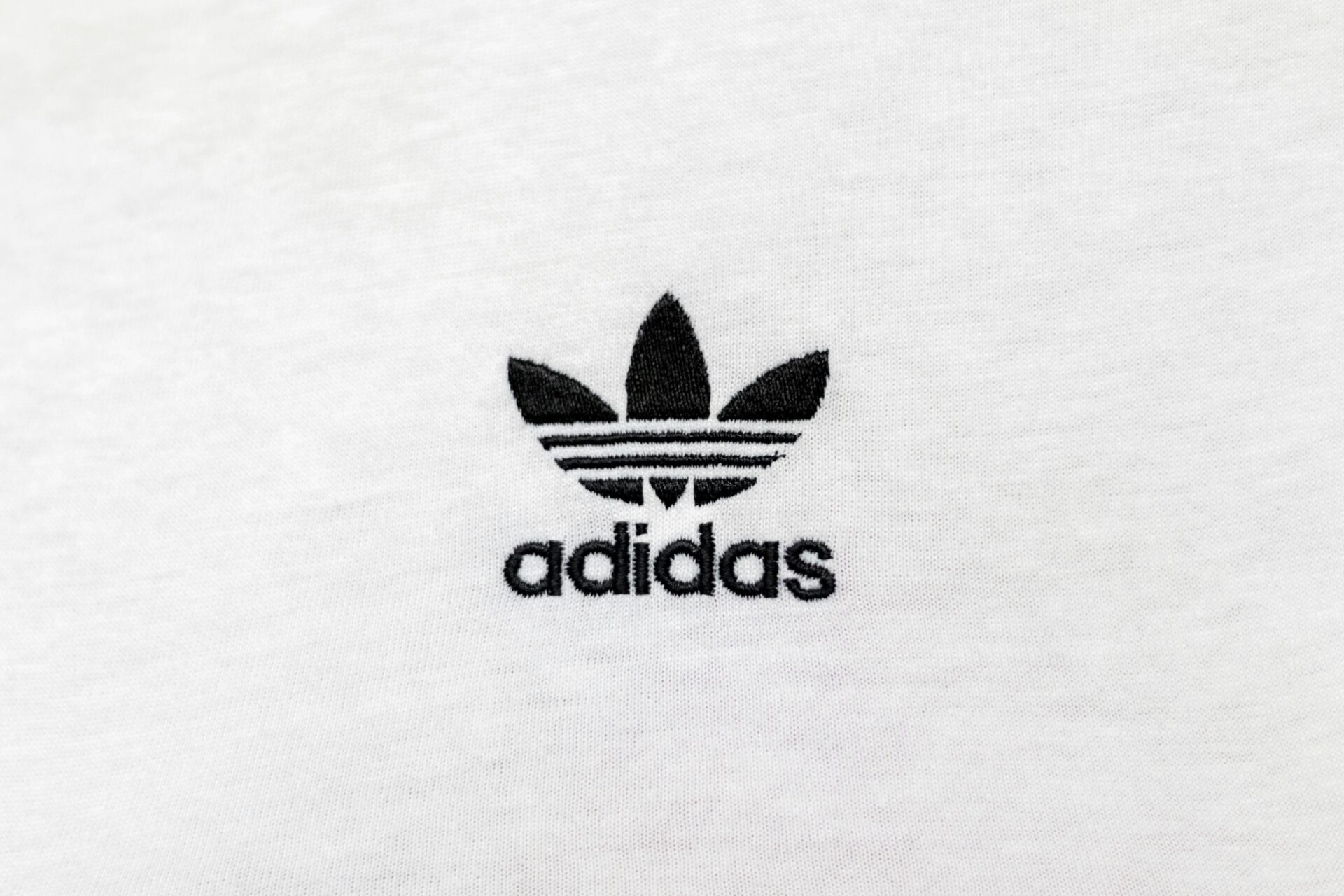 Logo marki Adidas na białym tle – przykład apelatywizacji, gdzie nazwa marki stała się synonimem butów sportowych w języku potocznym.
